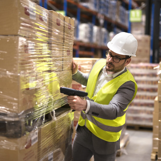 Male warehouse worker using bar code scanner to analyze newly arrived goods for further placement in storage department.